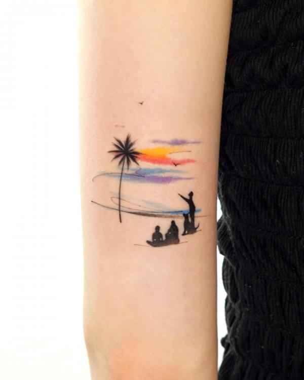 Tattoo of a family of four on a male forearm dad, mom and two boys around a  campfire. Background is a sunset at the bottom, night at the top with a big